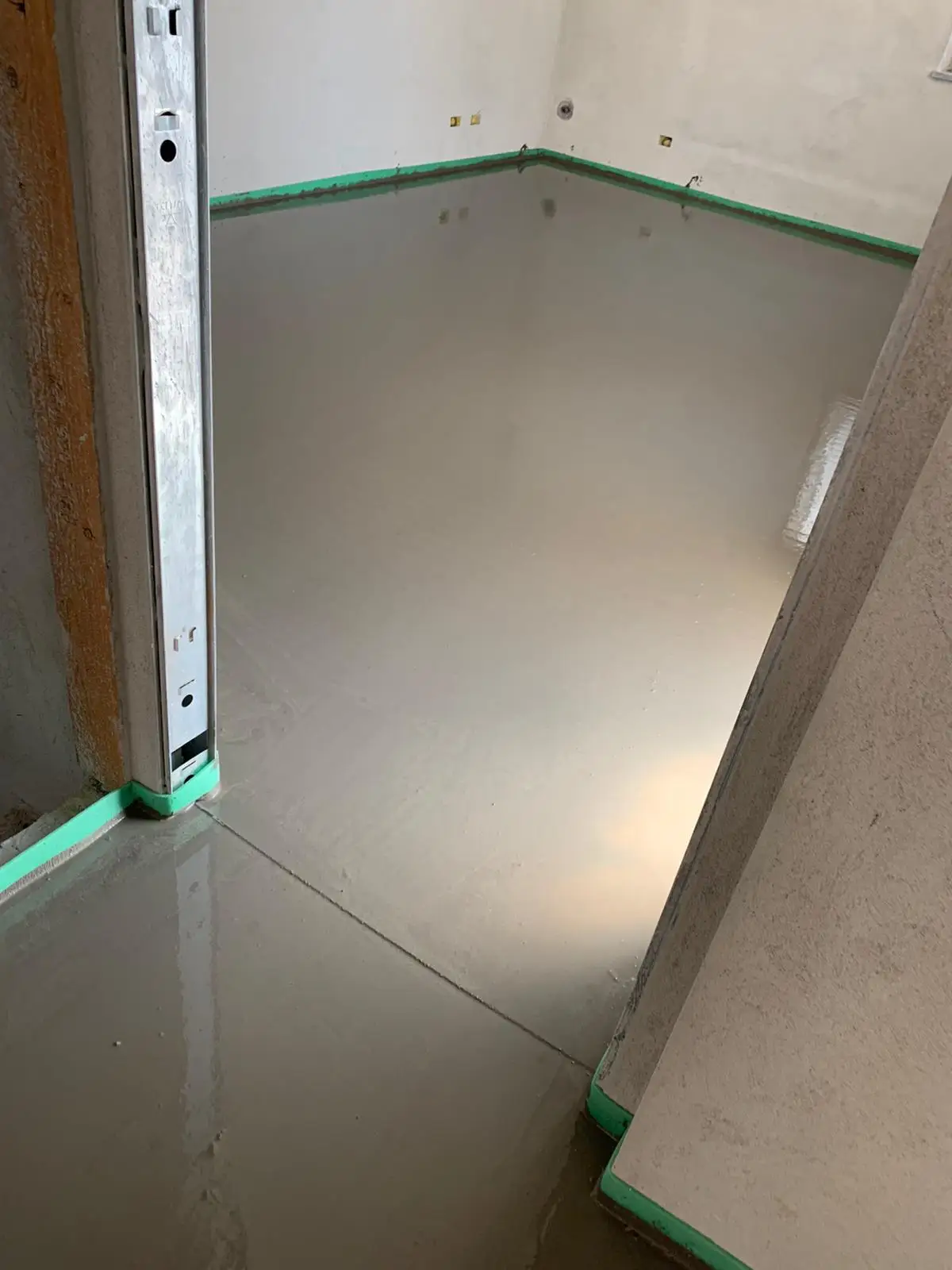 Superficie liscia del massetto tra due stanze, con fascia perimetrale verde e giunto sulla soglia.