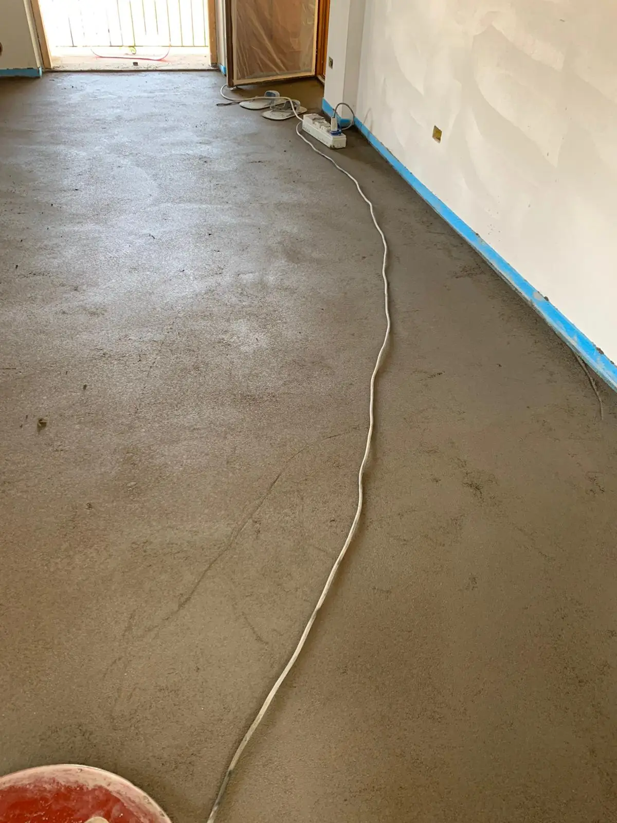 Cavo e frattazzatrice sul massetto di una stanza con fascia perimetrale azzurra.