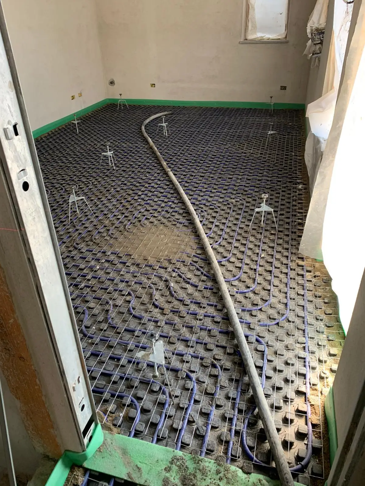 Tubazione di pompaggio sui pannelli sagomati del pavimento, con fascia perimetrale verde lungo le pareti.