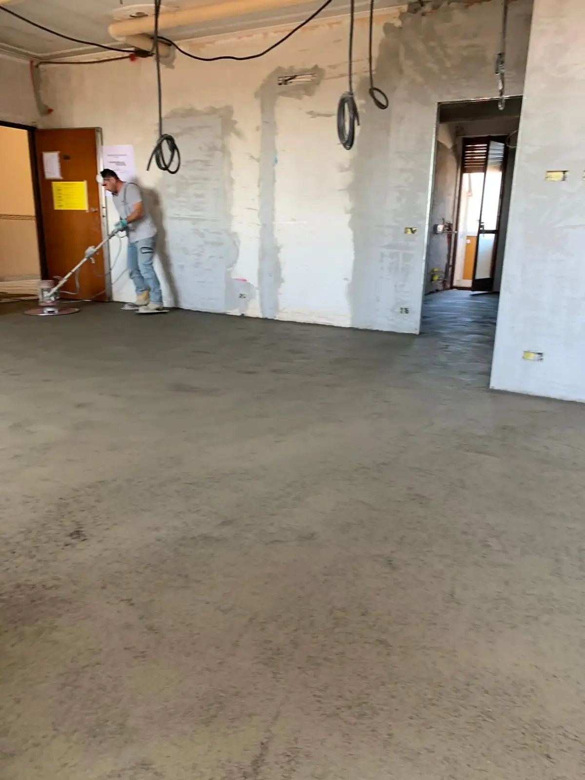 Operatore con attrezzatura di finitura sul massetto di un locale in ristrutturazione.