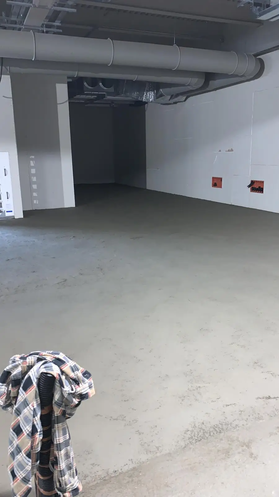 Massetto attorno a pilastri e pareti di un ampio ambiente con tubazioni a soffitto.