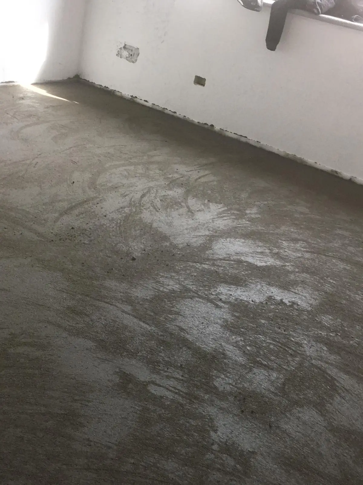 Dettaglio delle tracce di finitura del massetto lungo una parete con scatole elettriche.