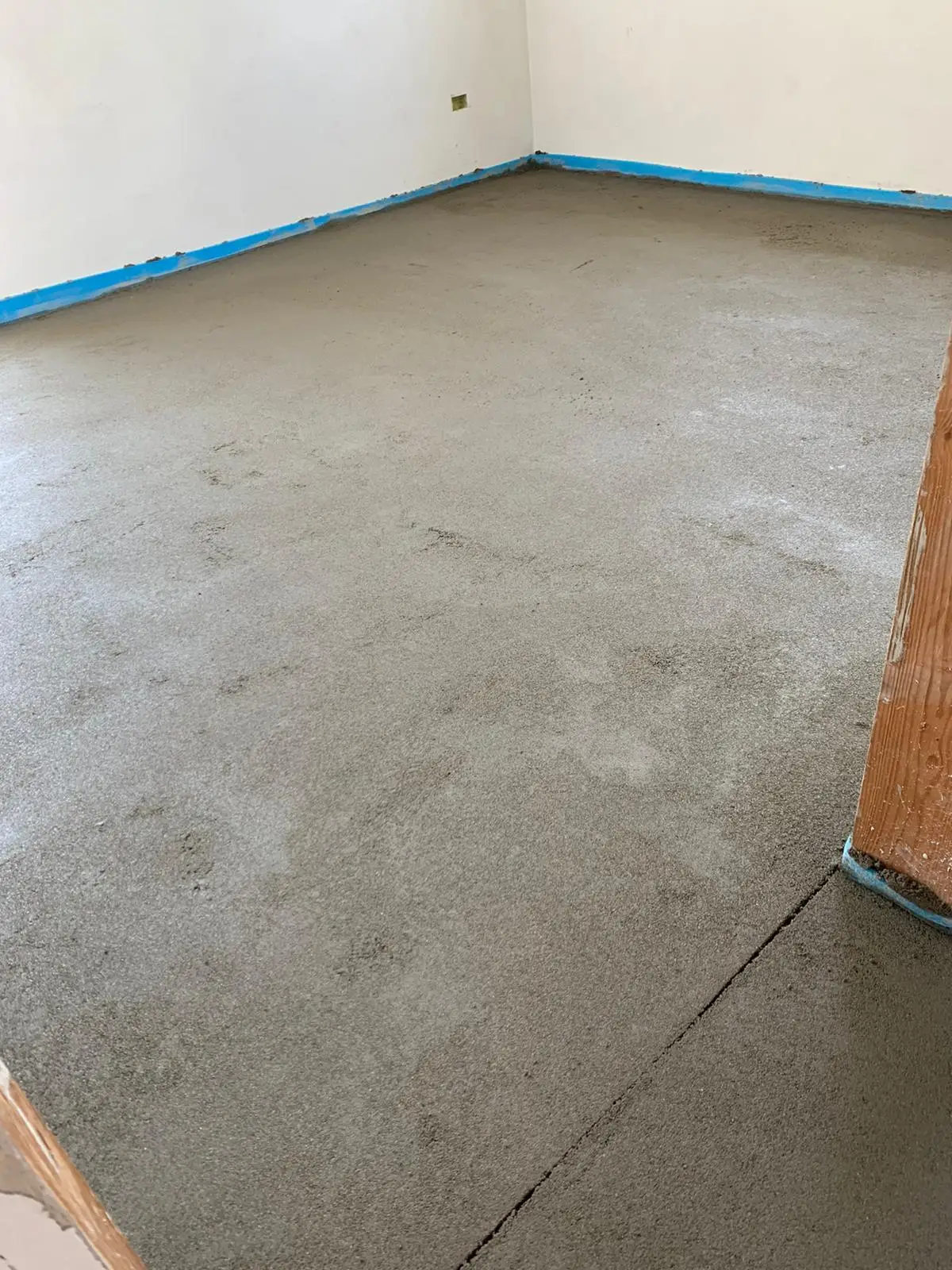 Superficie del massetto con un giunto visibile e fascia perimetrale azzurra lungo le pareti.