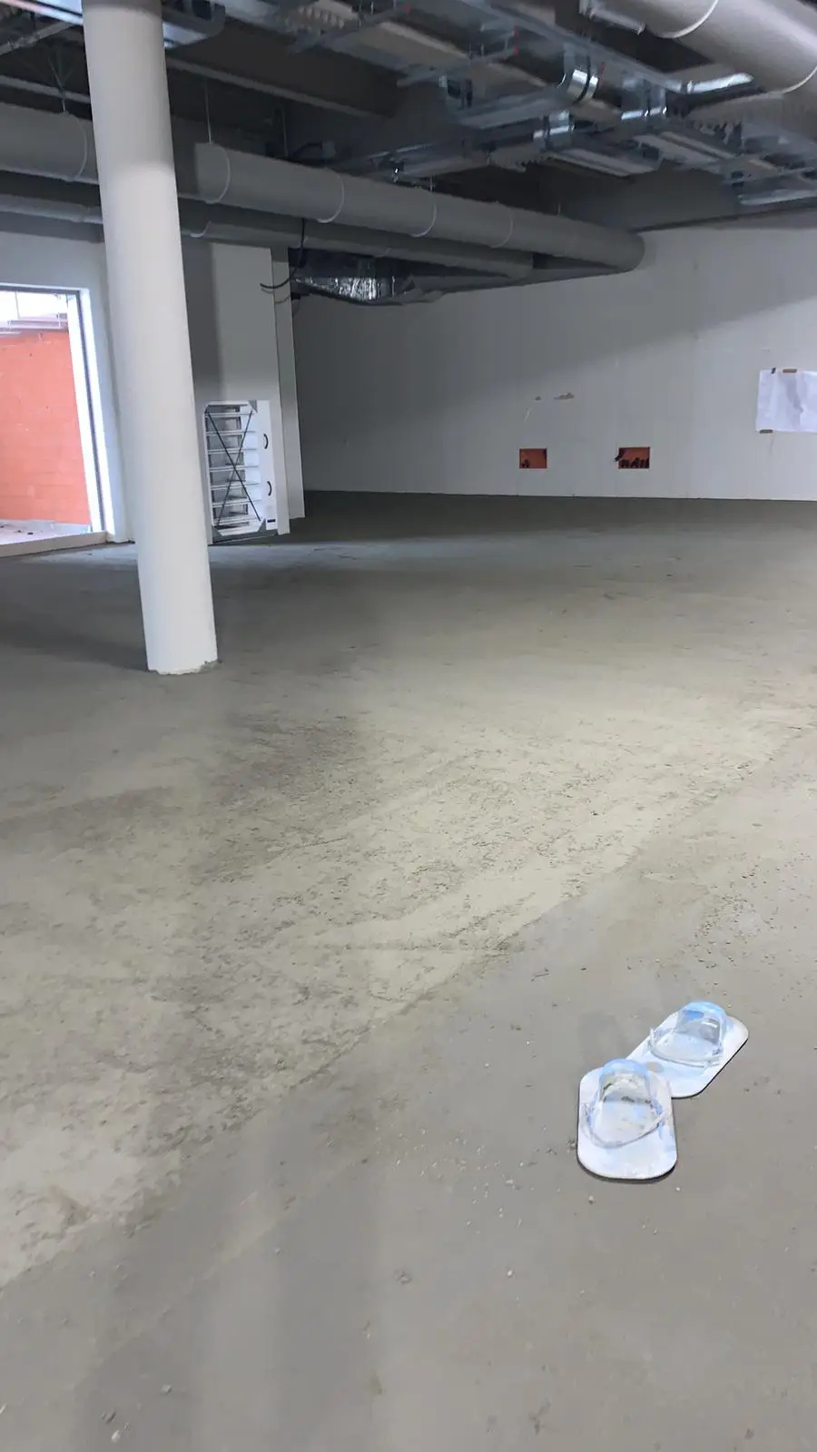 Superficie del massetto in un locale con pilastri, con calzature di cantiere in primo piano.