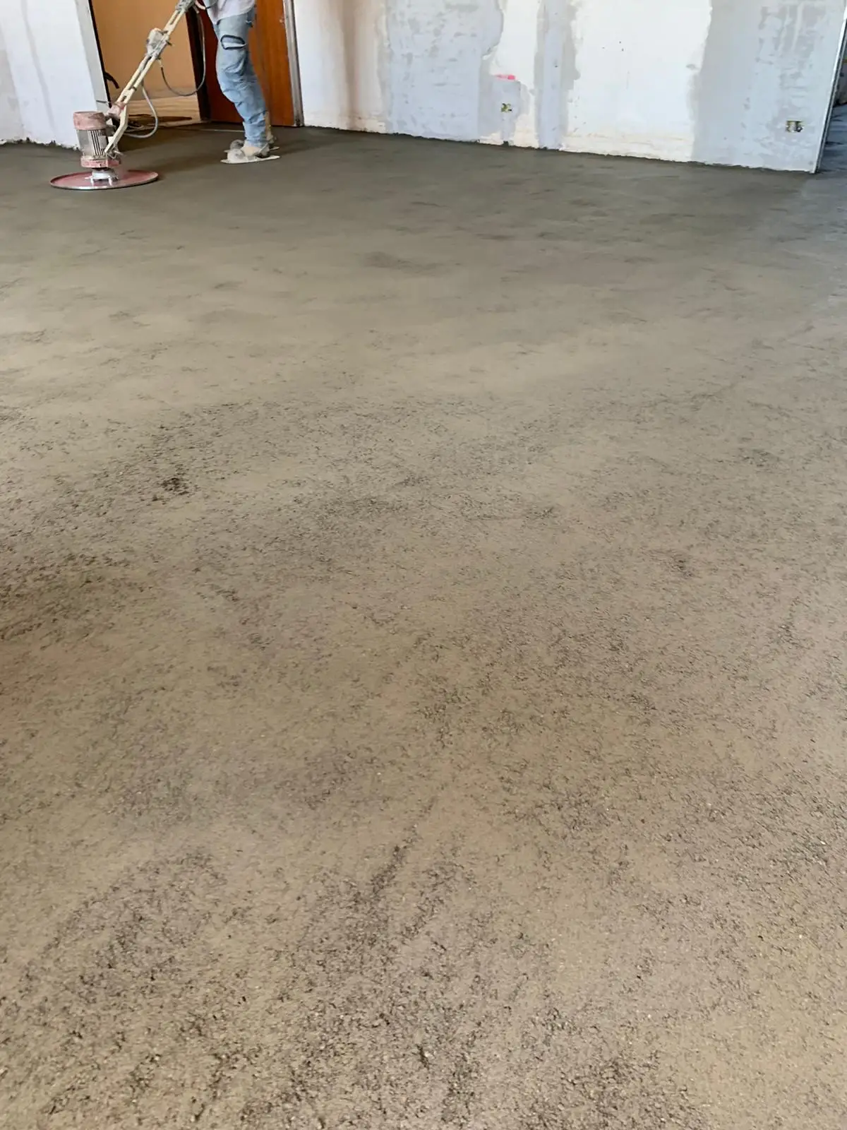 Superficie del massetto durante la lavorazione, con operatore e frattazzatrice sullo sfondo.